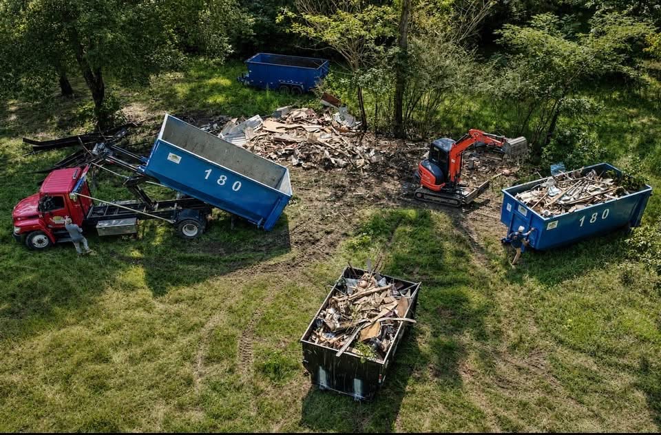 180 Junk Removal crews load demolition debris into roll-off dumpsters beside an excavator