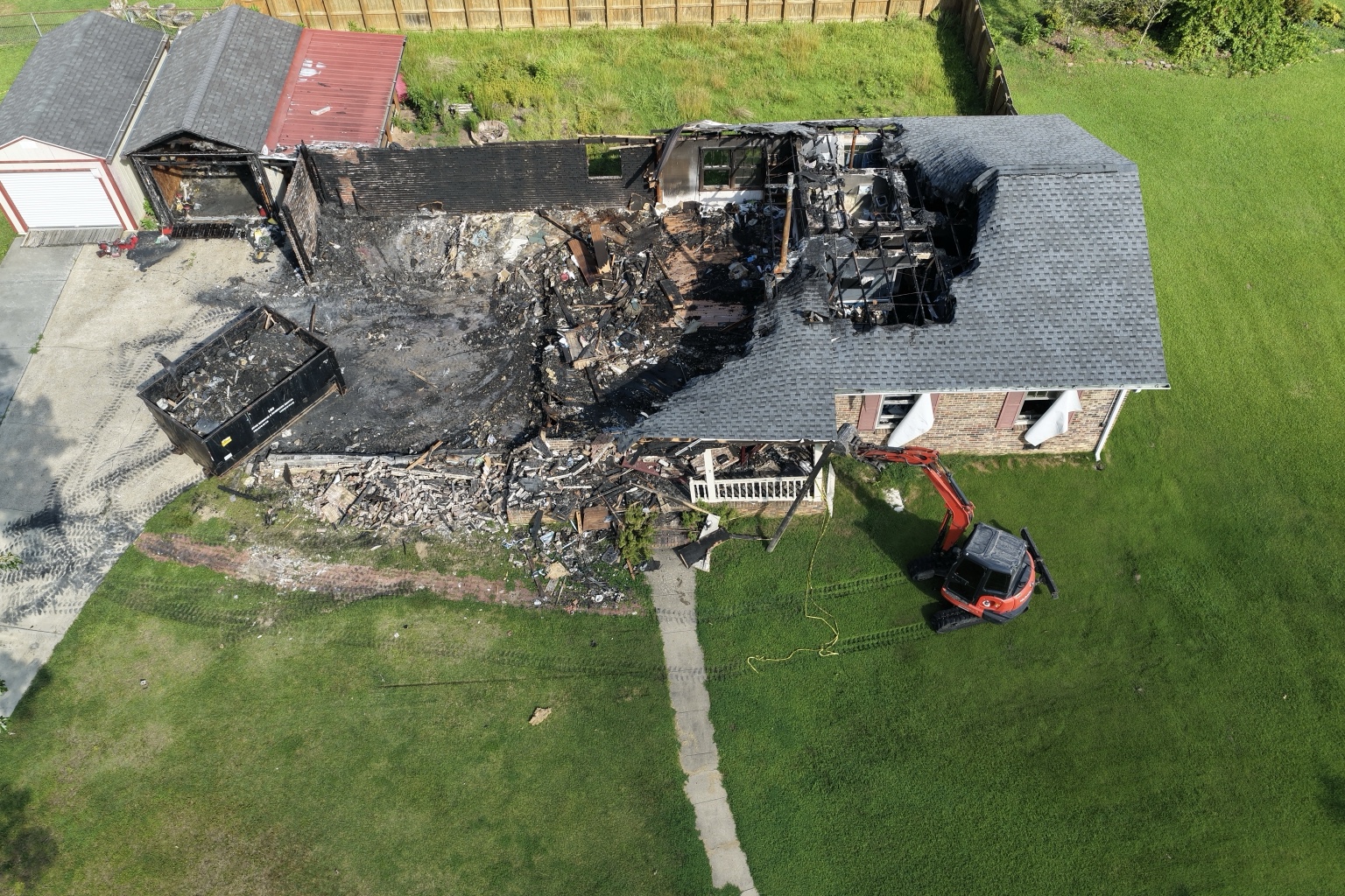 Aerial view of a fire-damaged house during demolition with an excavator beside it